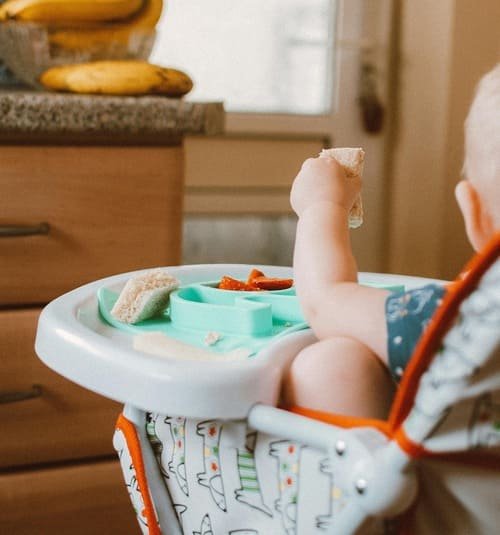 bebé desenfocado comiendo blw sentado en silla